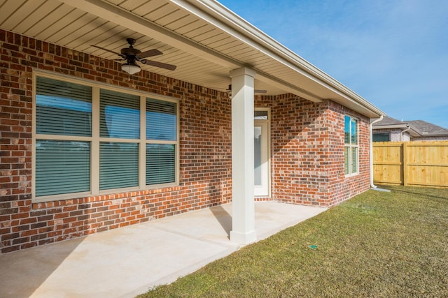 doorway to property featuring a lawn, brick siding, fence, and a ceiling fan