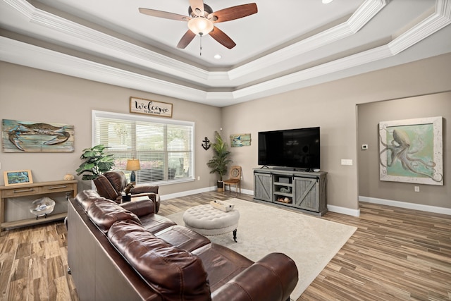 living room with baseboards, light wood-style floors, a ceiling fan, and a raised ceiling