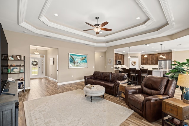 living area featuring a tray ceiling, crown molding, a ceiling fan, wood finished floors, and baseboards