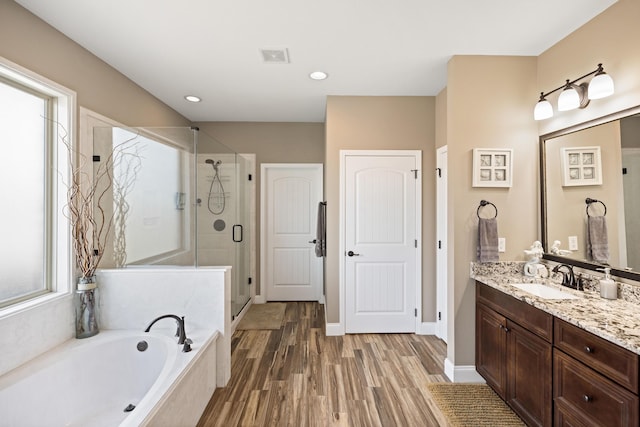 bathroom with vanity, a shower stall, wood finished floors, a bath, and visible vents