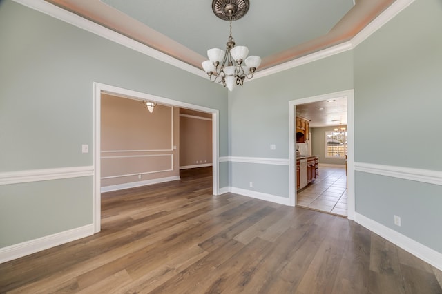unfurnished dining area with a notable chandelier, a tray ceiling, baseboards, and wood finished floors