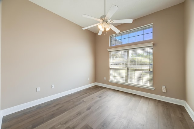 empty room featuring a ceiling fan, a wealth of natural light, baseboards, and wood finished floors