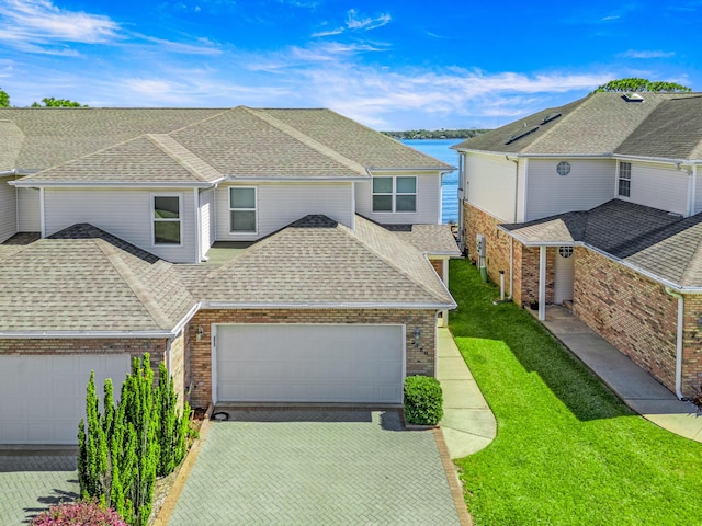 view of front of house featuring a front yard, driveway, a shingled roof, a garage, and brick siding