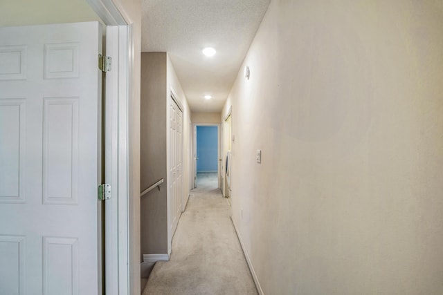hallway with light colored carpet, a textured ceiling, and baseboards