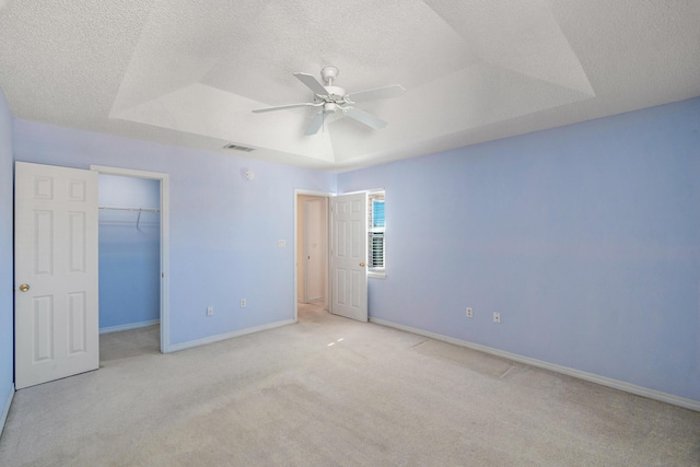 unfurnished bedroom featuring a raised ceiling, a textured ceiling, baseboards, light colored carpet, and ceiling fan