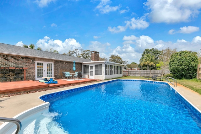 view of swimming pool featuring french doors, a fenced in pool, fence, a deck, and a sunroom