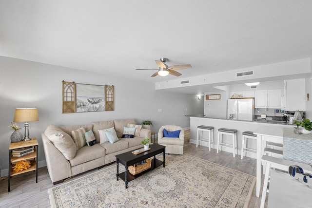 living area featuring light wood finished floors, baseboards, visible vents, and a ceiling fan