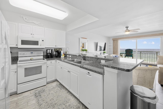 kitchen with white appliances, white cabinets, a sink, and a peninsula