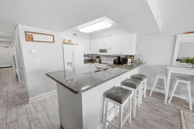 kitchen with white appliances, dark stone countertops, a breakfast bar, light wood-style floors, and a peninsula