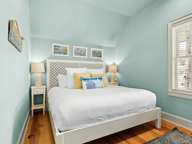 bedroom with baseboards, multiple windows, wood finished floors, and lofted ceiling
