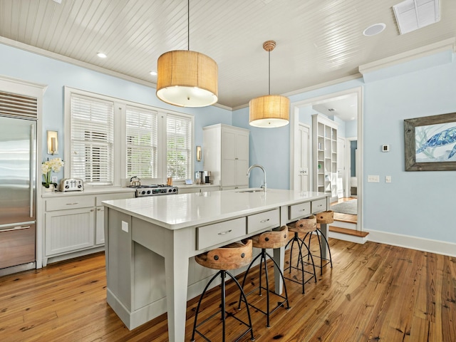 kitchen with light wood-style flooring, crown molding, stainless steel built in refrigerator, visible vents, and a kitchen bar