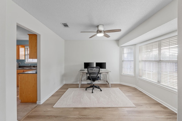 office area featuring visible vents, ceiling fan, a sink, light wood-type flooring, and a textured ceiling