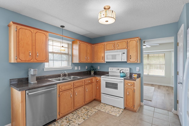 kitchen featuring a wealth of natural light, dark countertops, white appliances, and a sink