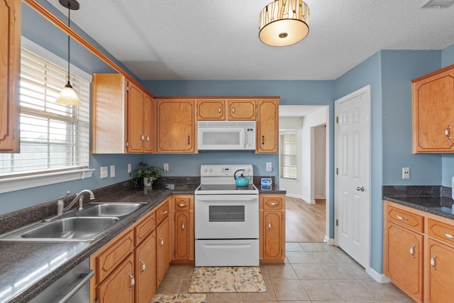 kitchen featuring a sink, white appliances, brown cabinetry, pendant lighting, and dark countertops