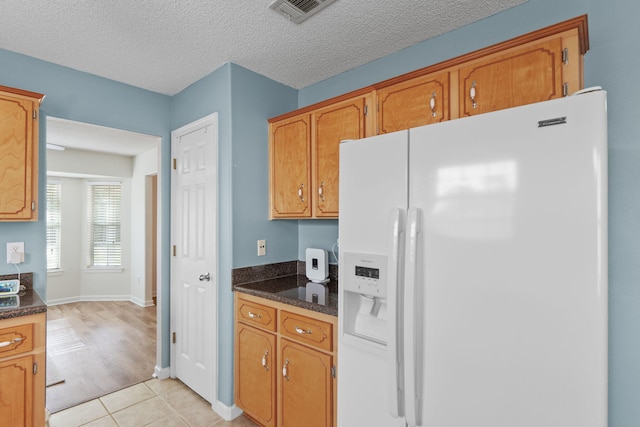 kitchen with white refrigerator with ice dispenser, light tile patterned floors, brown cabinets, dark countertops, and a textured ceiling