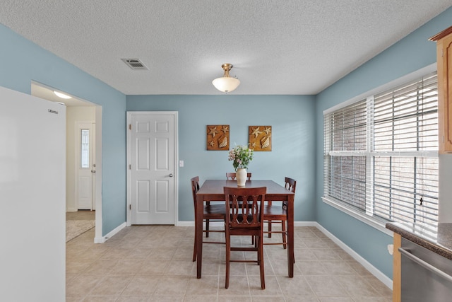 dining area with a textured ceiling, visible vents, light tile patterned floors, and baseboards