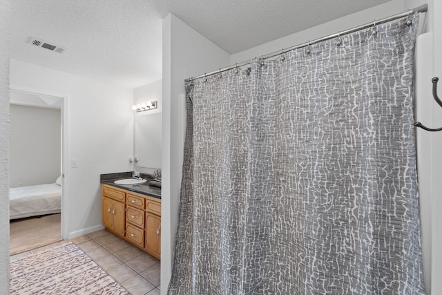 full bathroom featuring a textured ceiling, a sink, double vanity, visible vents, and tile patterned flooring