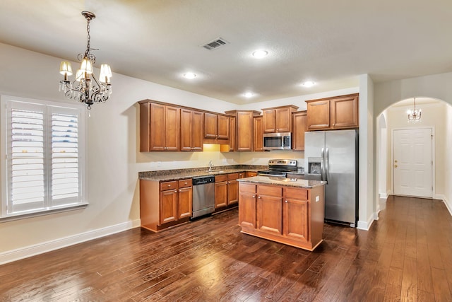 256 Cocobolo Dr, Santa Rosa Beach, FL 32459 - kitchen with arched walkways, a notable chandelier, brown cabinetry, dark wood-type flooring, and appliances with stainless steel finishes