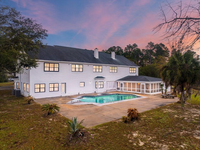 680 Mallet Bayou Rd, Freeport, FL 32439 - back of house at dusk featuring a patio area, a chimney, a sunroom, central AC unit, and an outdoor pool