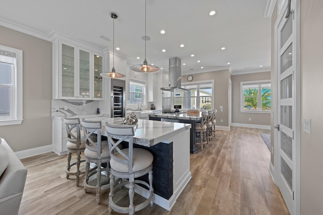 kitchen featuring island range hood, light wood-style flooring, ornamental molding, and a spacious island