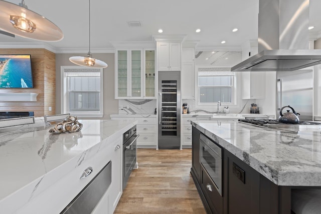 kitchen with white cabinetry, ornamental molding, island range hood, and appliances with stainless steel finishes