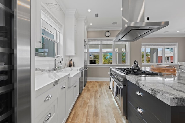 kitchen with island range hood, white cabinets, a sink, and high end stove