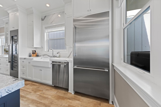 kitchen with white cabinets, a sink, appliances with stainless steel finishes, and light wood-type flooring