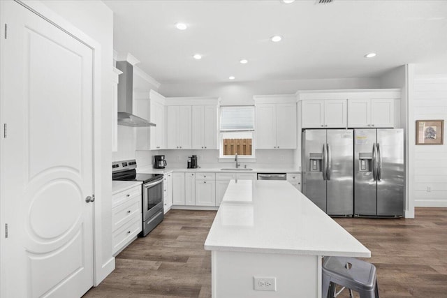 kitchen with wall chimney exhaust hood, a kitchen breakfast bar, a kitchen island, a sink, and stainless steel appliances