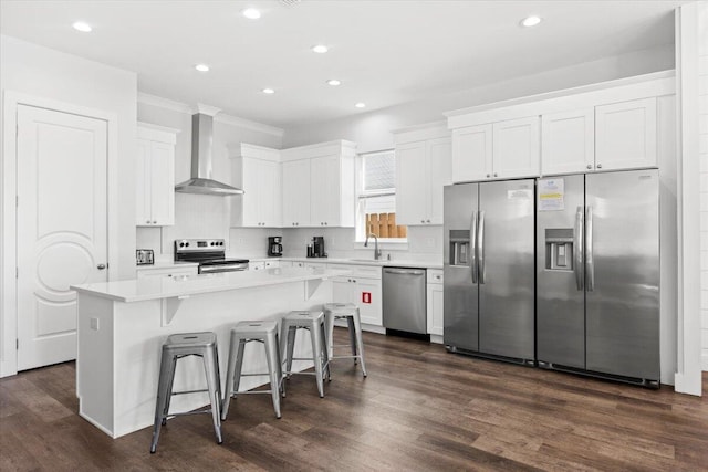 kitchen featuring white cabinets, a center island, wall chimney exhaust hood, and appliances with stainless steel finishes