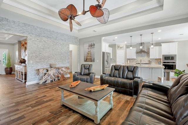 living area featuring a tray ceiling, ornamental molding, recessed lighting, wood finished floors, and baseboards