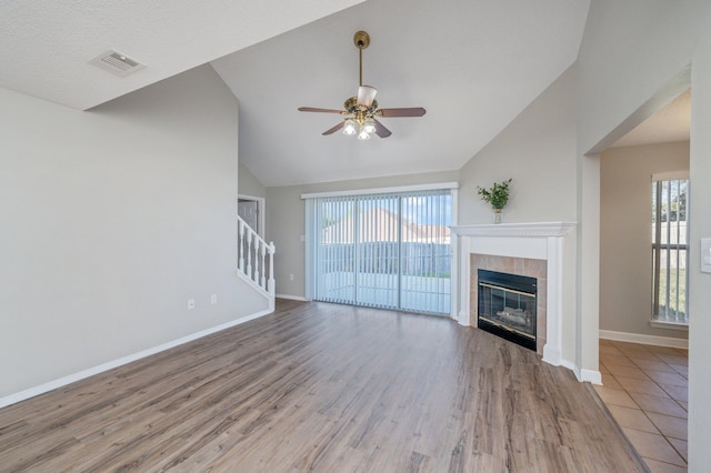 unfurnished living room with visible vents, ceiling fan, a tile fireplace, and wood finished floors