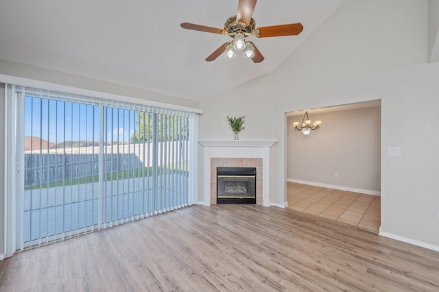 unfurnished living room featuring high vaulted ceiling, baseboards, a fireplace, wood finished floors, and ceiling fan with notable chandelier