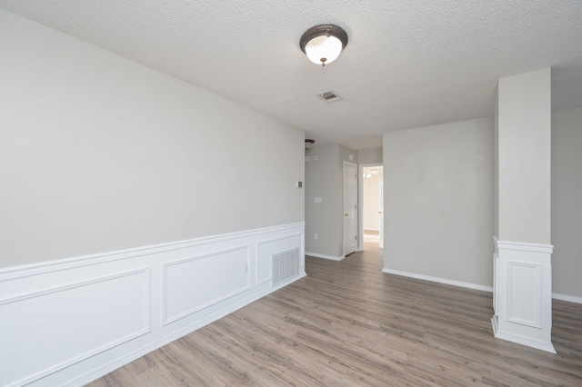 unfurnished room with a wainscoted wall, a textured ceiling, visible vents, and wood finished floors