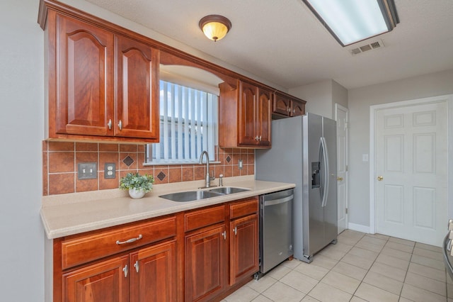 kitchen with light countertops, light tile patterned floors, decorative backsplash, a sink, and appliances with stainless steel finishes