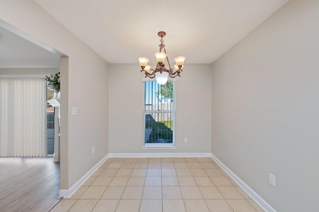 spare room featuring baseboards, a textured ceiling, light tile patterned flooring, and a notable chandelier