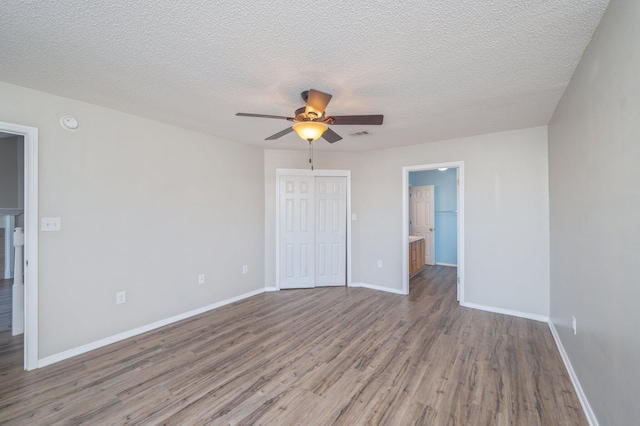 unfurnished bedroom with a closet, wood finished floors, a textured ceiling, baseboards, and visible vents