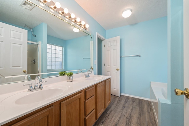 bathroom featuring wood finished floors, a sink, a shower with door, and visible vents