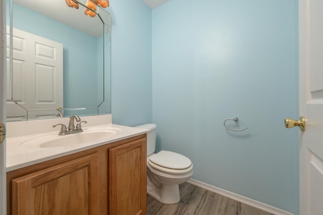 half bath with toilet, vanity, baseboards, and wood finished floors