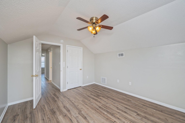 additional living space with visible vents, wood finished floors, lofted ceiling, and a textured ceiling