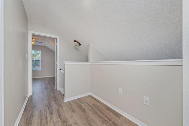 corridor featuring an upstairs landing, vaulted ceiling, baseboards, a textured ceiling, and wood finished floors