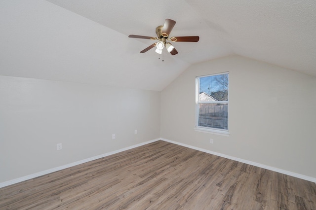 additional living space featuring vaulted ceiling, baseboards, a textured ceiling, a ceiling fan, and wood finished floors