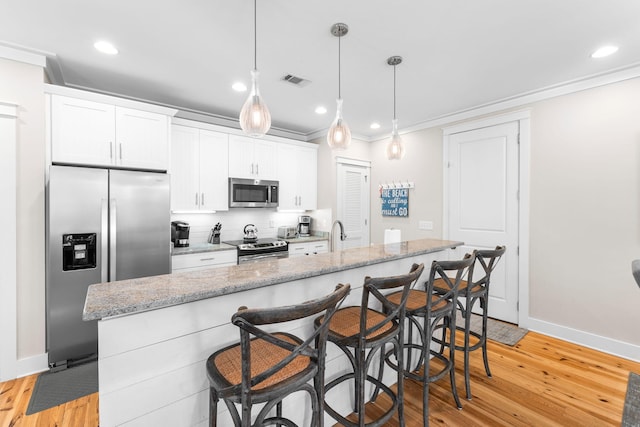 kitchen with a kitchen bar, ornamental molding, visible vents, and stainless steel appliances