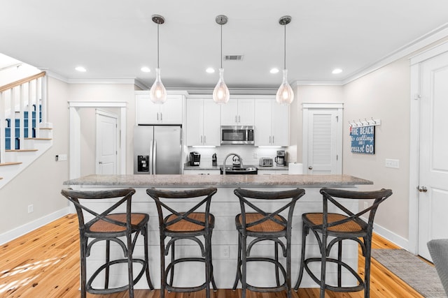 kitchen with a breakfast bar area, ornamental molding, an island with sink, visible vents, and appliances with stainless steel finishes