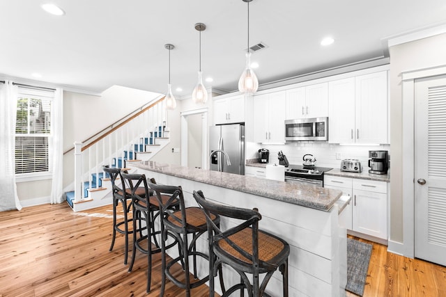 kitchen featuring backsplash, white cabinetry, appliances with stainless steel finishes, and light wood-style floors