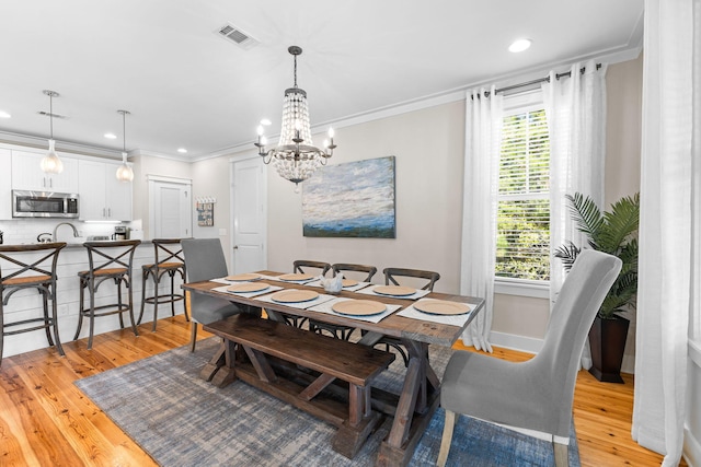 dining area featuring light wood-type flooring, crown molding, visible vents, and a chandelier