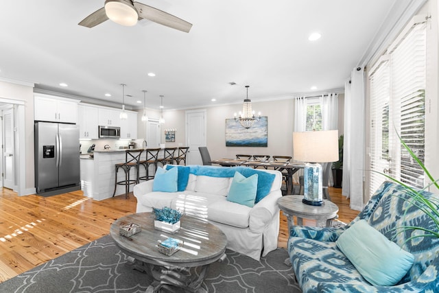 living room featuring recessed lighting, light wood-style floors, crown molding, and ceiling fan with notable chandelier