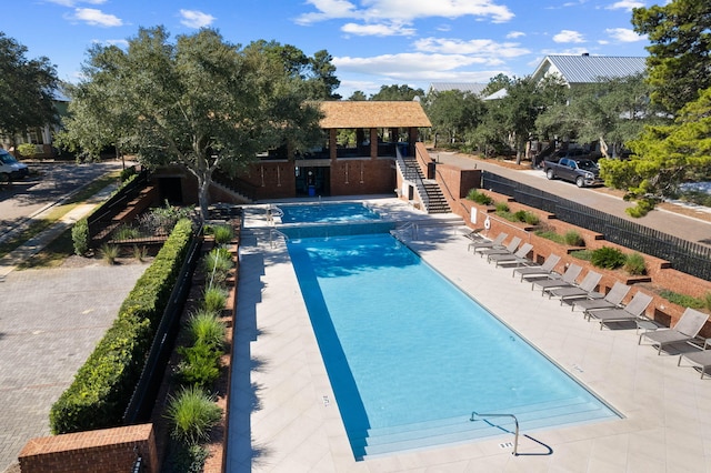 community pool featuring a patio area, stairs, and fence