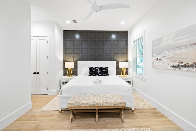 bedroom with baseboards, a decorative wall, visible vents, and light wood finished floors