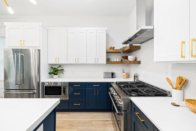 kitchen featuring white cabinets, high quality appliances, wall chimney exhaust hood, and blue cabinetry