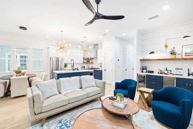 living room featuring light wood finished floors, wine cooler, bar area, recessed lighting, and ceiling fan with notable chandelier
